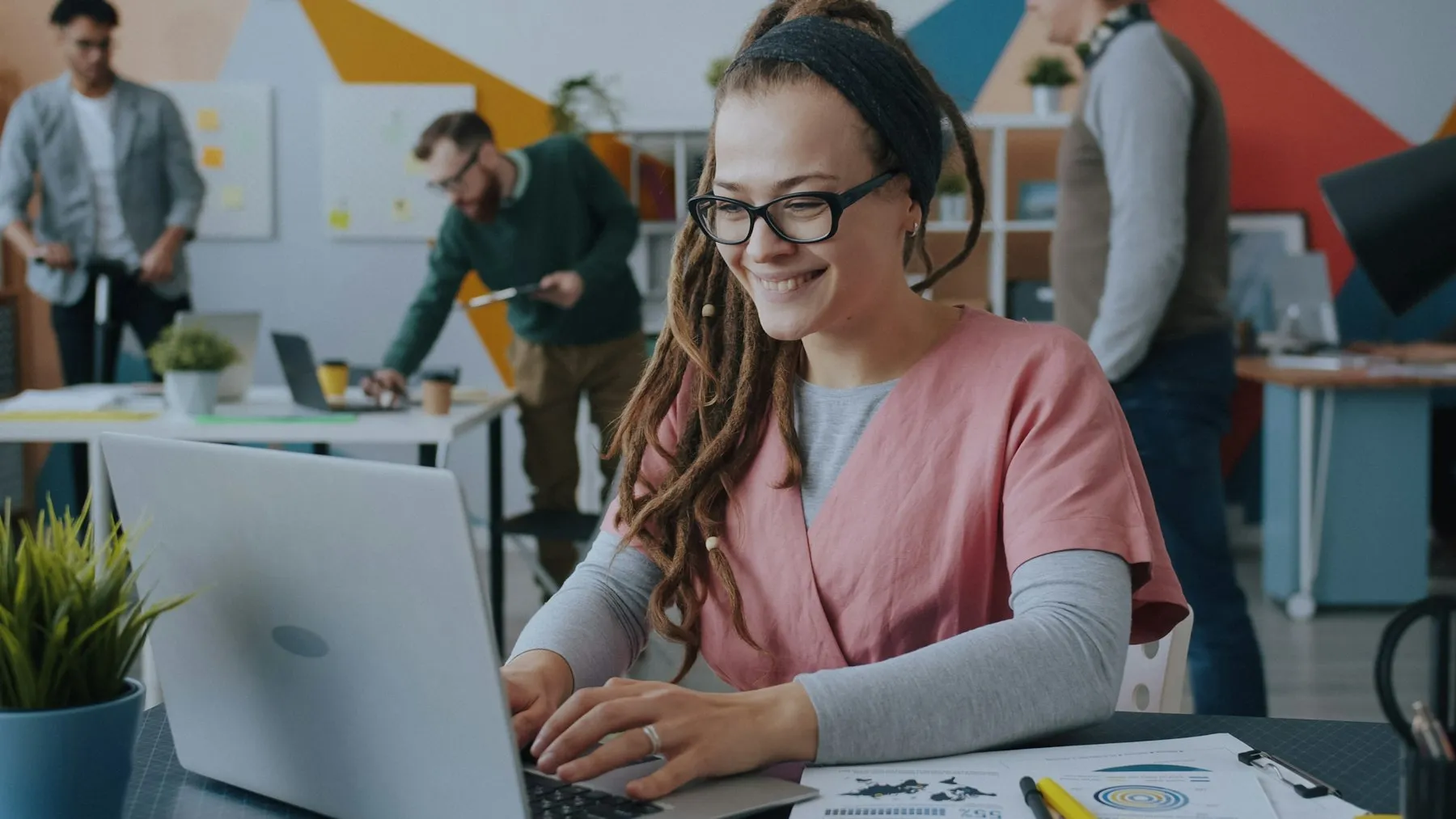 Smiling professional typing on a laptop in a busy office