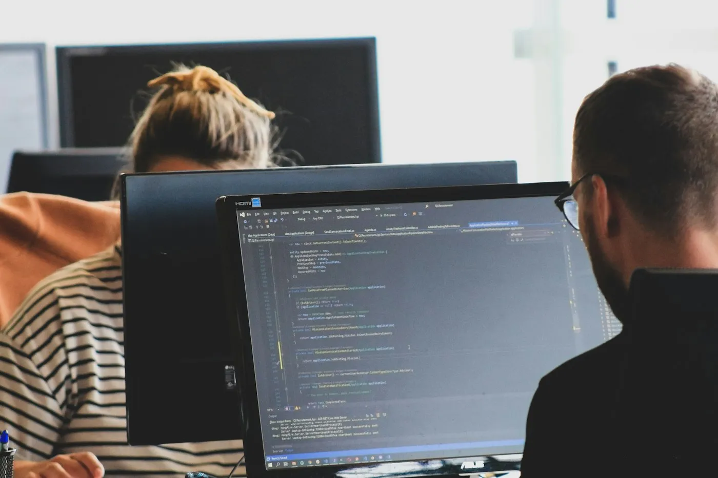 Two engineers reviewing code on large monitors